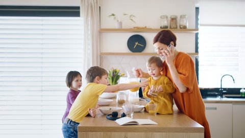 Mother with small children and smartphone in kitchen in the morning at home, eating breakfast.
