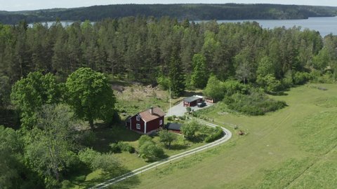 Swedish cabin by forest and lake. Red wooden house in drone shot. Lovely summer time in Sweden. Flag waving on pole. Beautiful peaceful idyllic farm landscape aerial view