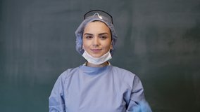 Female Doctor or Nurse Wearing Scrubs and Protective Mask and Goggles Banner. The doctor smiles and looks at the camera. 4K slow motion video.