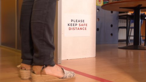 Woman waiting behind a red line to enter a classroom. Social distancing measures for the reopening and adaptation of schools and academies to the new normal.