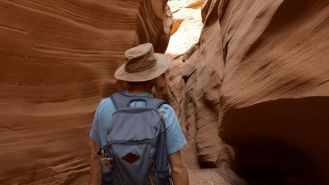 Young man walking inside narrow canyon in the desert, waving his hand inviting companion to follow him. Tracking shot, pov couple enjoying hike inside Antelope Canyon, USA