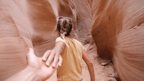 Young adventurous couple holding hands woman leading boyfriend walking into narrow canyon in the desert POV travel concept. Female waving hand, inviting partner to follow her 