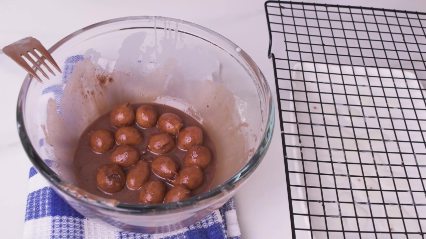 Drying donut holes with chocolate glase on wire rack on blue rag over white marble side view
