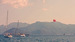 People with parachute above sea with yachts. Parasailing. Parachute with Turkish flag pattern. 4K raw video record.