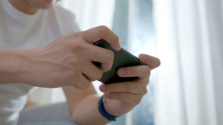 Close up asian man's hand playing online game via smartphone digital gadget at living room. Happy male feeling funny and excite with win competition game e-sport entertainment network.Self-quarantine | Shutterstock HD Video #1053873818