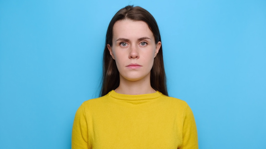 Portrait of scared young woman peep through fingers feel frightened terrified, stares with widely opened eyes, wears yellow sweater, hides face from someone, isolated on blue studio background Royalty-Free Stock Footage #1053874790