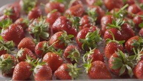 Tracking slow motion video of a wet ripe red strawberry with green leaves on a square tray with holes from stainless steel. Soft focus. Shallow depth of field. Full HD video, 240fps,1080p