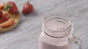 Slow motion of a strawberry milk smoothie, woman's hand puts chia seeds, a leaf of mint and plastic straws in a jar with milk cocktail. Slow motion. Full HD video, 240fps,1080p.