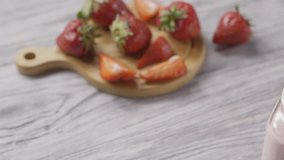 Slow motion panoramic full HD video of a strawberry milk smoothie, coctail on gray table. Background from blurred strawberry fruit on a wooden board. Soft focus, close-up of glass cup. 240 fps, 1080p.