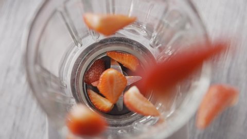Top view of the glass container of the blender, into which falls a red, ripe strawberry fruit for making smoothies, a cocktail. Healthy organic food. Full HD video, 240fps,1080p.