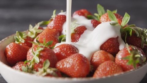 A close-up of a white bowl with a large ripe red strawberry and milk yogurt pouring onto the berries with a splash. Slow motion video. Full HD video, 240fps,1080p.