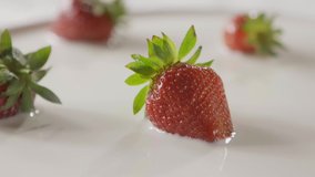 Slow motion of a falling splash of milk to the ripe red strawberry fruit on plate. On a white plate is few berries in the milk. Close-up background, soft focus. Full HD video, 240fps,1080p.