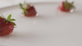 Slow motion of a falling drops of water and ripe red strawberry fruit to a plate with water splashes. On a white plate is few berries. Close-up background, soft focus. Full HD video, 240fps,1080p.