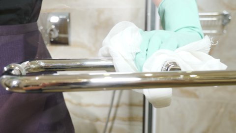 Cleaning chrome-plated bathrooms, bidets. polishing crane and handles. Cleaning in hotel. Close-up shot of maid from hotel staff wiping bath handles, bathtub in toilet at residential building . Shot