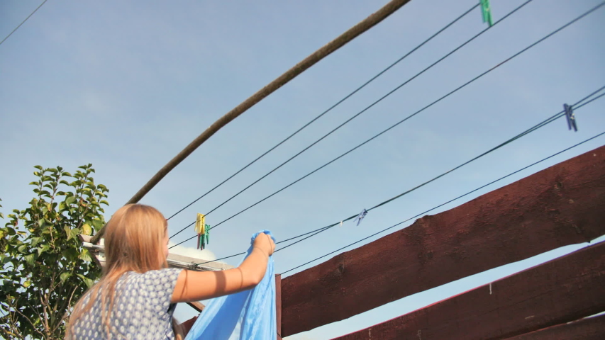 A young mom hangs out lingerie outdoors on a sunny day.