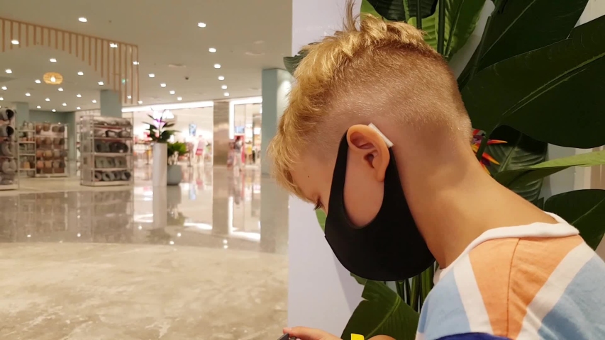 Lttle boy in mask sits in a shopping center