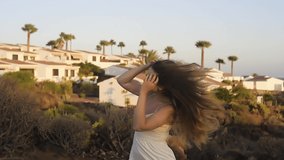The girl dances in the mountains, against the backdrop of the ocean and the tourist city. Gorgeous brown-haired woman with long hair dancing, music video, summer. Sunset on the island.	
