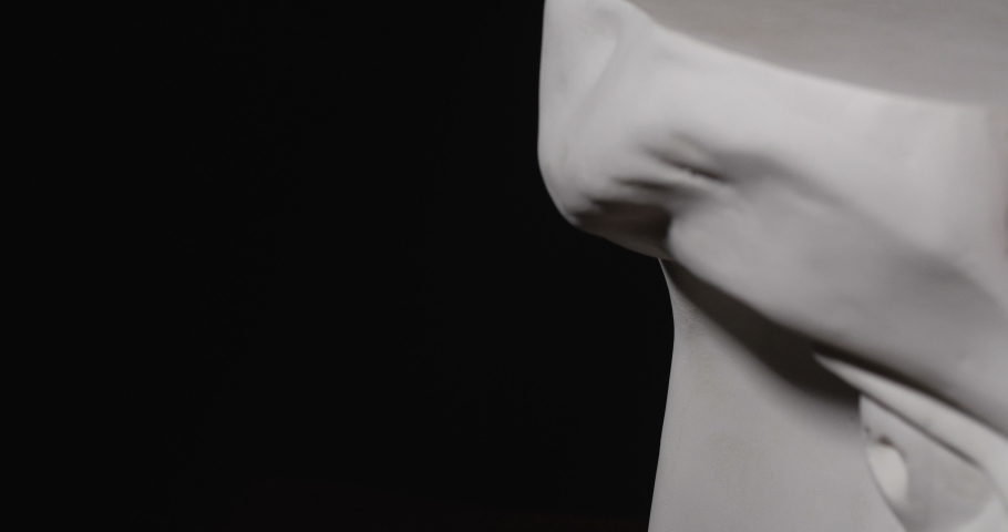 Epic studio close-up shot of a gypsum head with dramatic lighting. The play of light and shadow on half the face of a white statue of a man. Stern eyes. On a black background isolated 4k