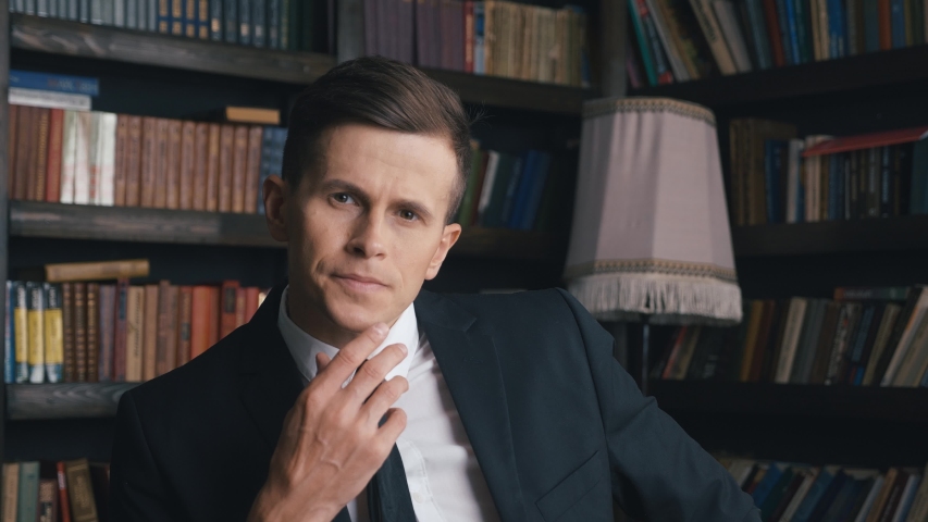Portrait of handsome confident young businessman in the office. Wearing classic suit. male employee executive face succesed with good job career on the background of bookshelf.