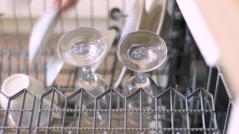 Young Woman Arranging Plates In Dishwasher At Home, Open dishwasher with clean dishes in the white kitchen