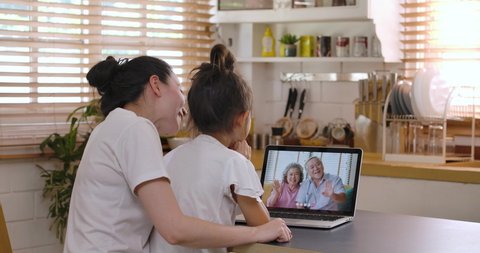 Happy yound asian mother and daughter video calling old senior parents talking with grandparents mom dad in webcam conference chat application on laptop screen on table. Family videocall concept.