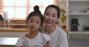 Cheerful young Asian mom and daughter talking video calling from home. Happy beautiful family adult single mother parent and cute little girl chatting online in virtual app by web camera.