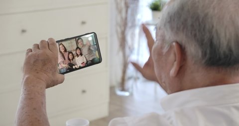 Over shoulder closeup view of asian senior elderly 70s man user holding smart phone watching mobile video calling family in virtual app, older grandparent learn using modern technology gadget concept.