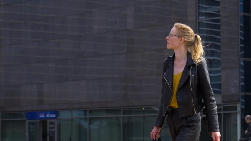 Young relaxed woman walking down the street and looking around. Female with glasses calmly goes to work.