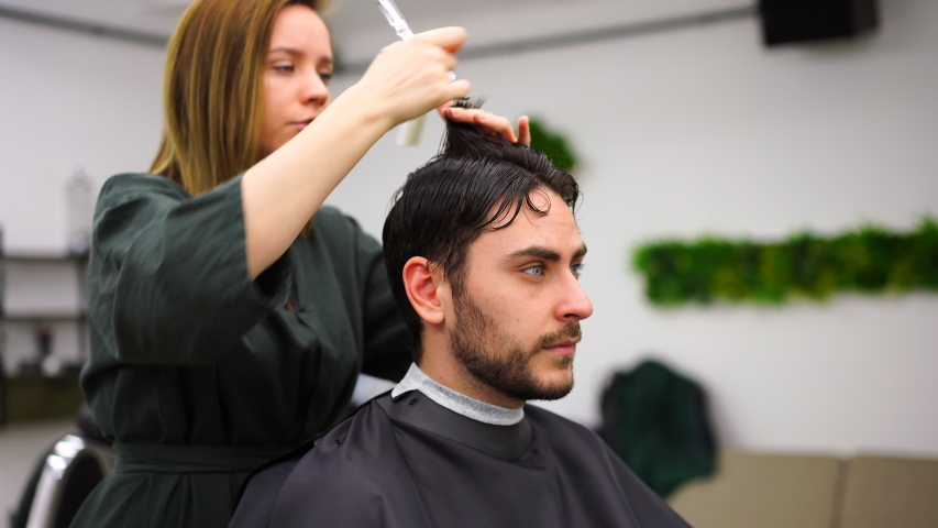 Stylish man sitting barber shop Hairstylist Hairdresser Woman cutting his hair Portrait handsome happy young bearded caucasian guy getting trendy haircut Attractive barber girl working serving client  | Shutterstock HD Video #1053897122