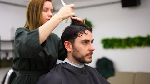 Stylish man sitting barber shop Hairstylist Hairdresser Woman cutting his hair Portrait handsome happy young bearded caucasian guy getting trendy haircut Attractive barber girl working serving client 