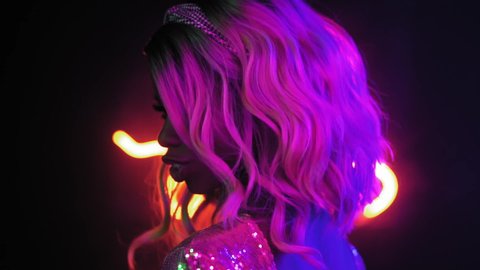 Close up. Sensual blond girl dancing in semi lit light studio. African American girl dancing in studio in neon abstract lighting in a silver shining dress. Neon concept. Slow motion. Prores 422. 