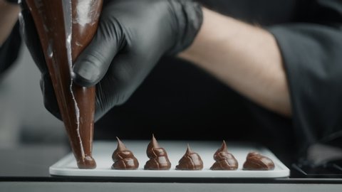 Chef chocolatier makes sweets from melted chocolate with pastry bag in slow motion, raw materials for making filling for truffles, cooking the sweet desserts, making candies, 