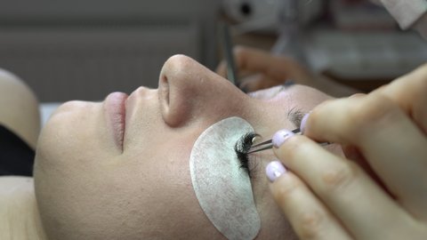 Woman eye with long curvy eyelashes. Young woman undergoing eyelash extensions procedure, closeup. The process of increasing and volumetric eyelash extensions to a girl.