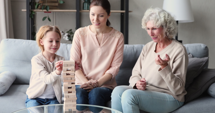 Excited little 6 or 7 years old cute redhead child involved in funny build board game with smiling young mother and happy senior older granny, building wooden tower and taking out blocks at home. Royalty-Free Stock Footage #1053902228