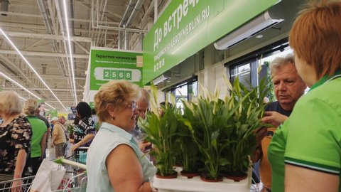 KAZAN, TATARSTAN/RUSSIA - SEPTEMBER 21 2019: Smiling saleswoman in green uniform t-shirt gives fresh pot plants to customers as compliment near modern supermarket exit on September 21 in Kazan