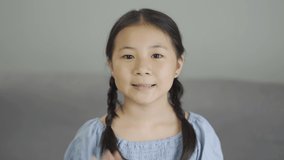 Cute asian little girl smiling and waving hand looking at camera at home