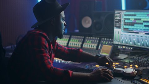Stylish Male Audio Engineer / Producer Working in Music Recording Studio, Uses Mixing Board and Software to Create Hit Track. Portrat of Creative Black Artist Musician Using Control Desk.