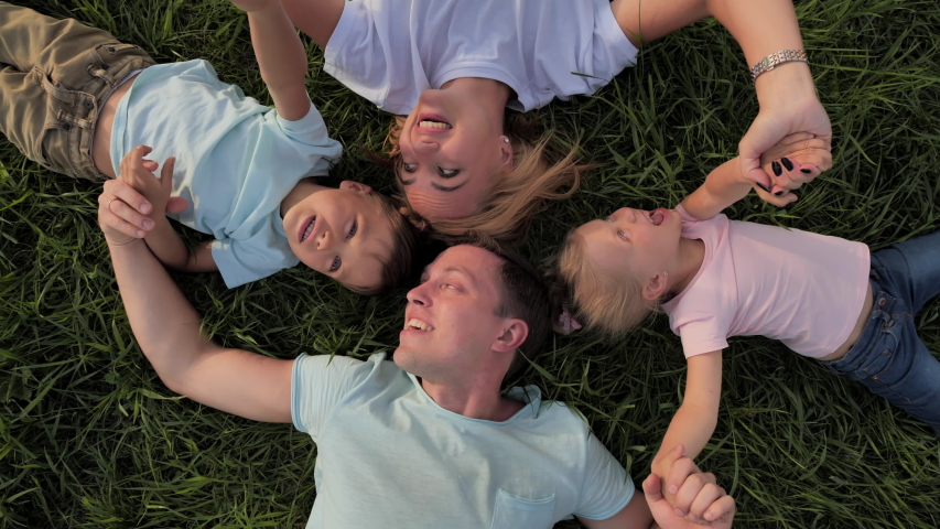 The camera rotates on a close-up of mother, father and children who are lying on the lawn with their heads touching each other, they hold hands, grimace and laugh merrily.
