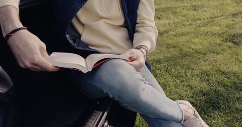 a young man in sunglasses reads a book and is relaxed at sunset on the edge of a forest, park.