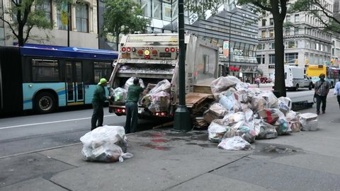 MANHATTAN, NYC - OCTOBER 09, 2019: Garbage Truck in NYC and two DSNY workers Loading White Plastic Garbage Trash Bags into Truck. Manhattan