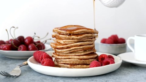 Syrup pouring on pancakes. Stack of american pancakes served with raspberry, cherry and maple syrup. Tasty sweet breakfast food