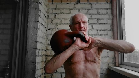 Man 80s 90s years old lifts dumbbell kettlebell up. Workout by gaffer oldster retiree inside balcony of the apartment at home. Sports and fitness. Healthy life. Morning exercise for caucasian man