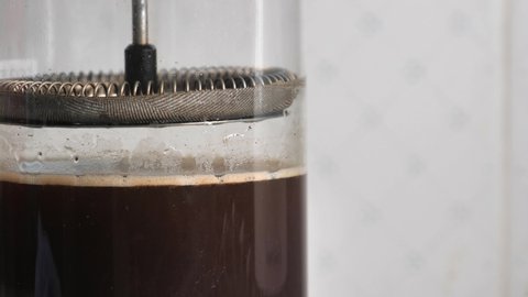 Slow motion of french press filter plunger going slowly into water with coffee grind causing bubbles and liquid to bounce. Macro close up.