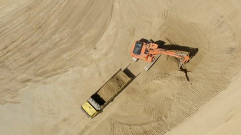 Top aerial shot: tractor bucket is filling a truck body. A excavator and truck are loading soil. Preparing place to construction residential house. 4K