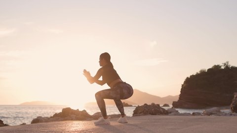 sporty woman squats workout on beach. Beautiful fitness model butt workout outdoors. Sunset beach with sea view background.