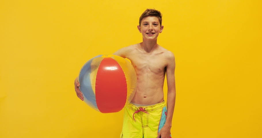 Happy excited teen guy standing with a beach ball isolated on a yellow background Royalty-Free Stock Footage #1053953522