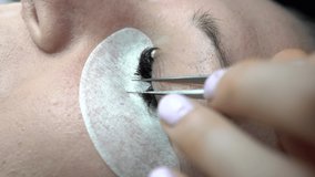 Skillful cosmetologist increases eyelashes with a volumetric method in a beauty salon. The process of increasing and volumetric eyelash extensions to a girl. Gluing false lashes with a tweezers.