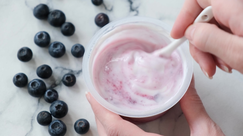 Blueberry greek yogurt in jar. Person stirring blueberry filling with natural greek yogurt in plastic jar. Store bought blueberry yogurt Royalty-Free Stock Footage #1053966032