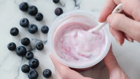 Blueberry greek yogurt in jar. Person stirring blueberry filling with natural greek yogurt in plastic jar. Store bought blueberry yogurt