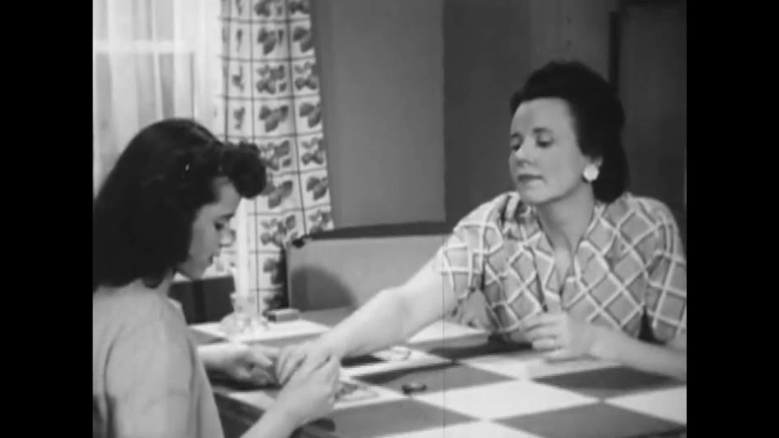 CIRCA 1940s - A woman gives her daughter instruction on identifying warp threads from filling threads in woolen fabrics in the 1940s.